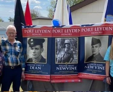 My dad Ed Newvine stands next to military banners honoring family members who served in the military. Chester T. Dean is memorialized with a banner honoring his service in World War II .